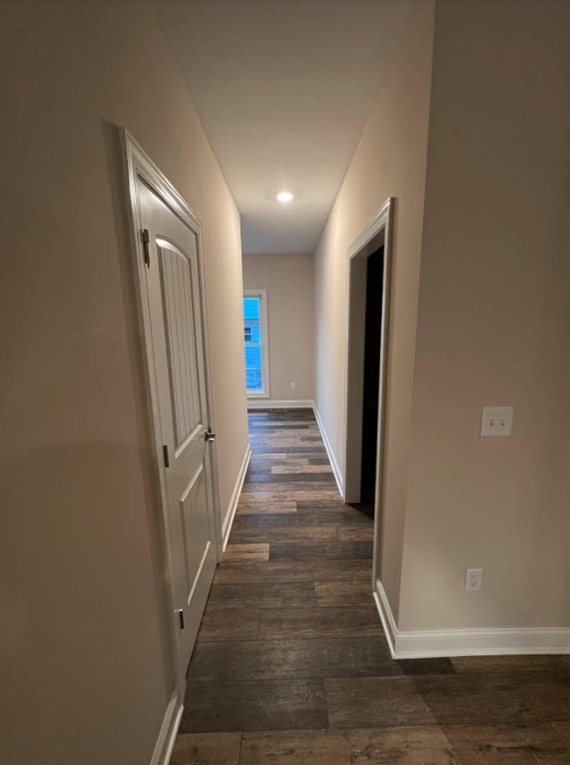 Hallway with white plaster walls, wood laminate flooring, white doors with silver handles, and a white light switch on the wall