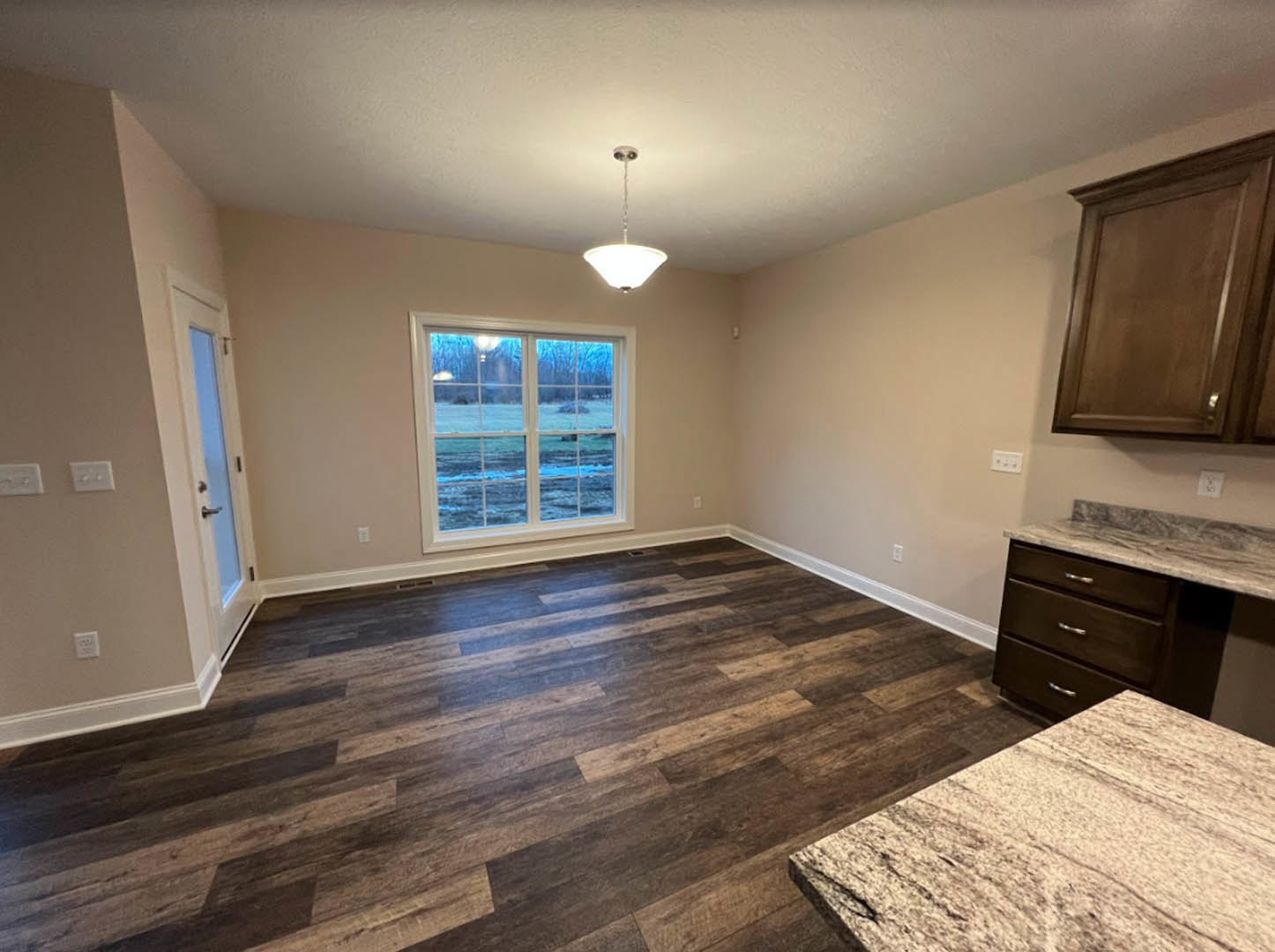 Marble countertop kitchen with hardwood flooring, white cabinetry, ceiling light fixture, window overlooking a field, and close-up details of door and countertop surfaces