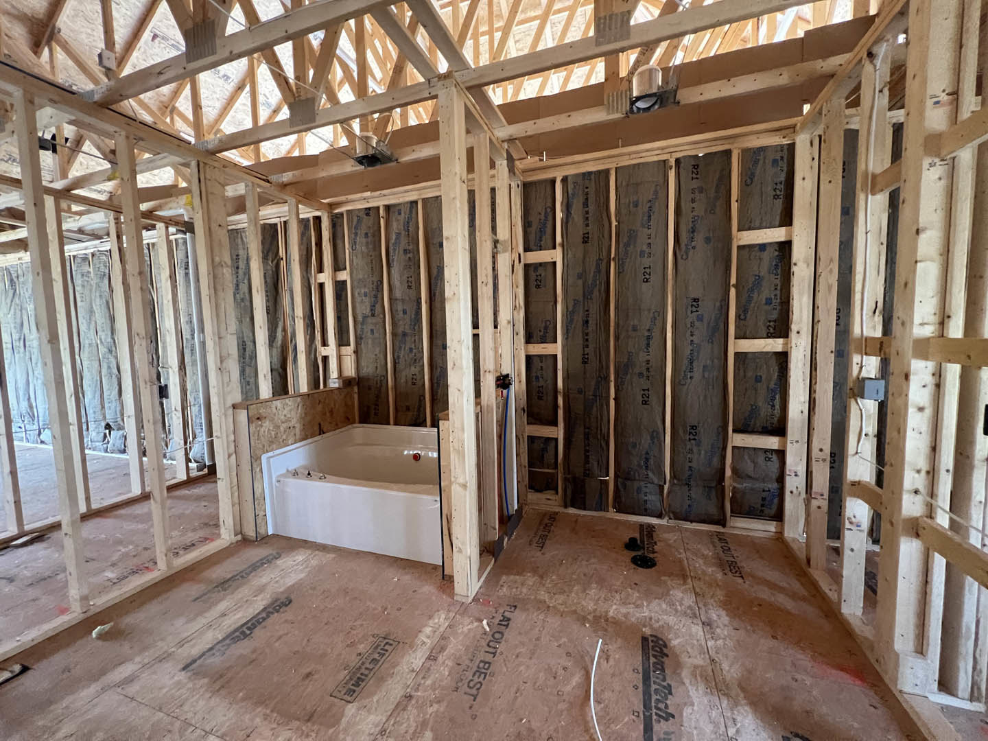 Bathroom under construction featuring exposed wood ceiling beams, plywood subfloor, bathtub, and walls with visible insulation