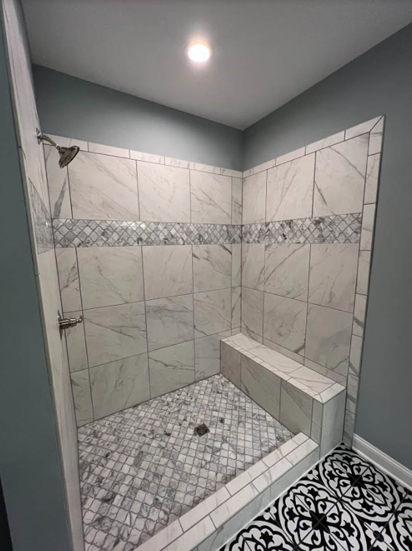Walk-in shower with built-in bench, black and white tile floor, marble wall tiles, ceiling light, and bathroom accessories