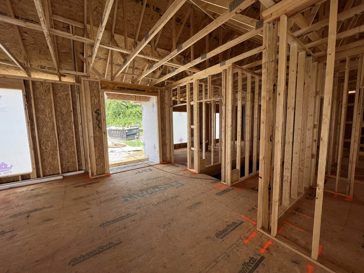 Wood-framed room under construction with exposed beams, white wall, window, and black dumpster filled with debris