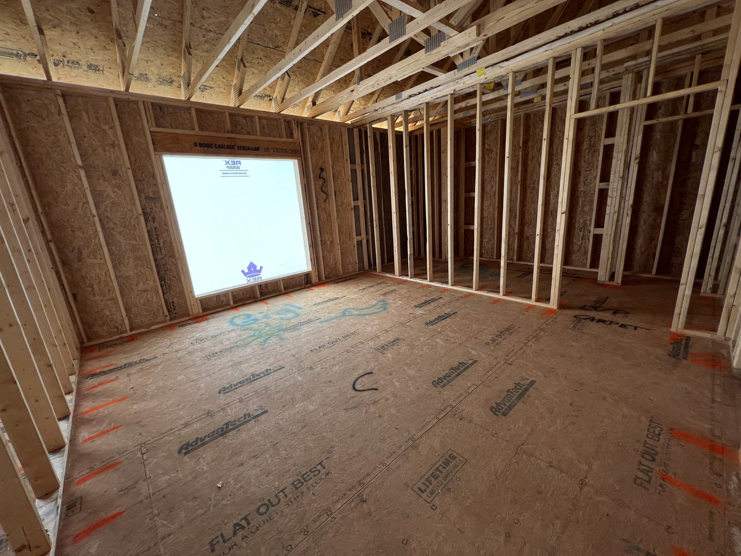 Exposed wood ceiling beams, white square window with wooden trim, light-colored walls, floor featuring black lettering