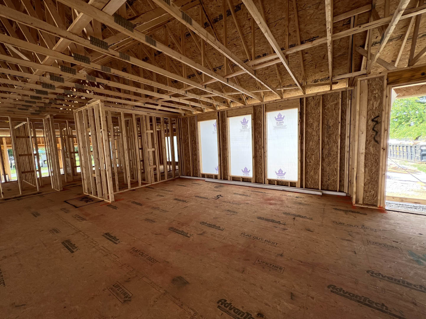 Open room with exposed wood ceiling beams, light hardwood flooring, white walls, and large windows letting in natural light