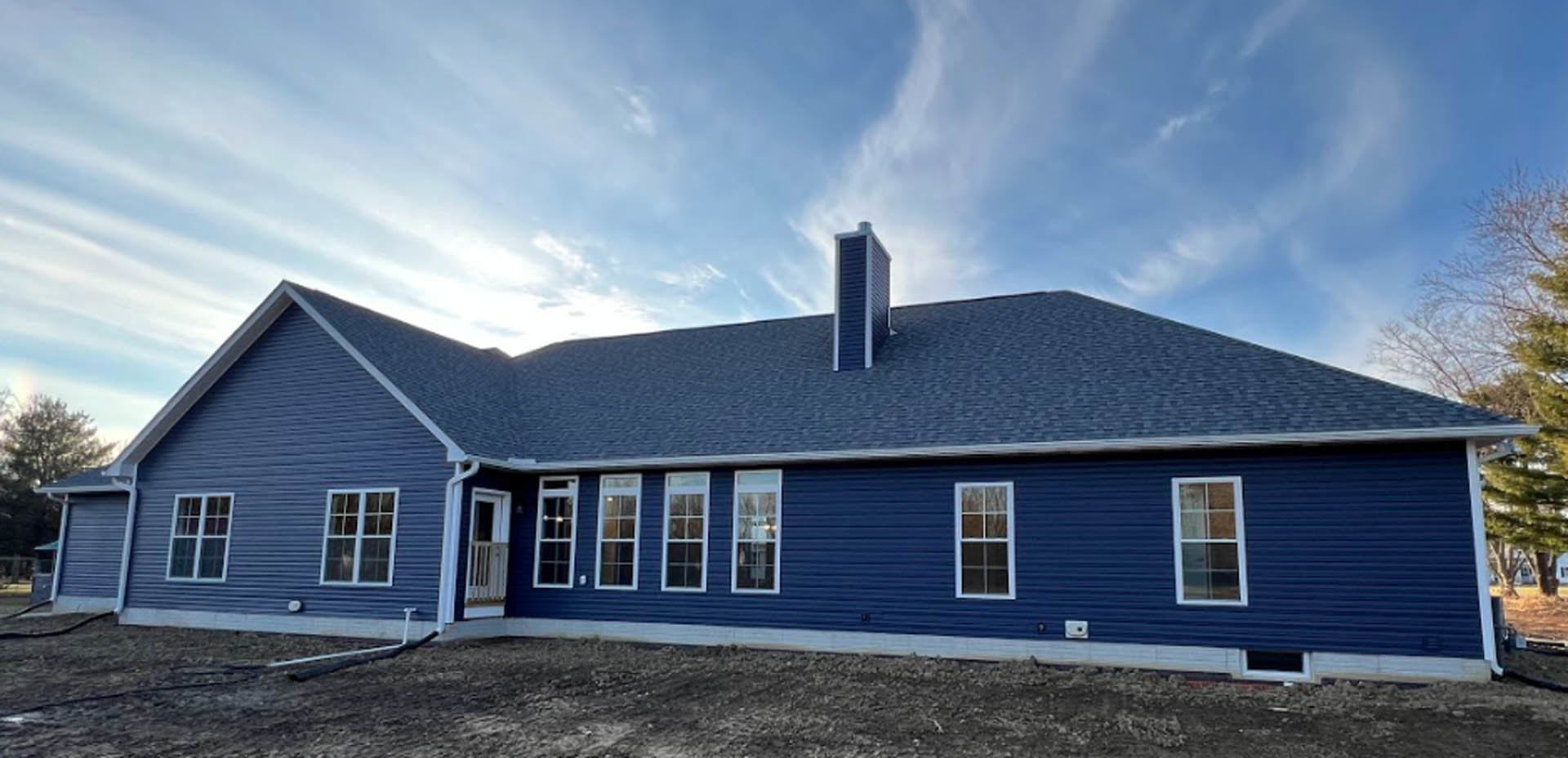 Blue siding house with matching blue roof, white framed multi-pane window, and brick chimney against a cloudy sky.