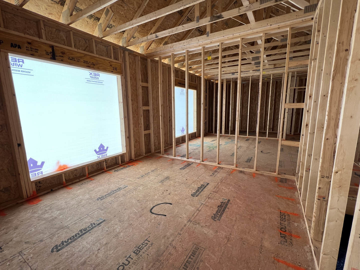 Exposed wood ceiling beams, large window with white trim, unfinished walls, light-colored flooring