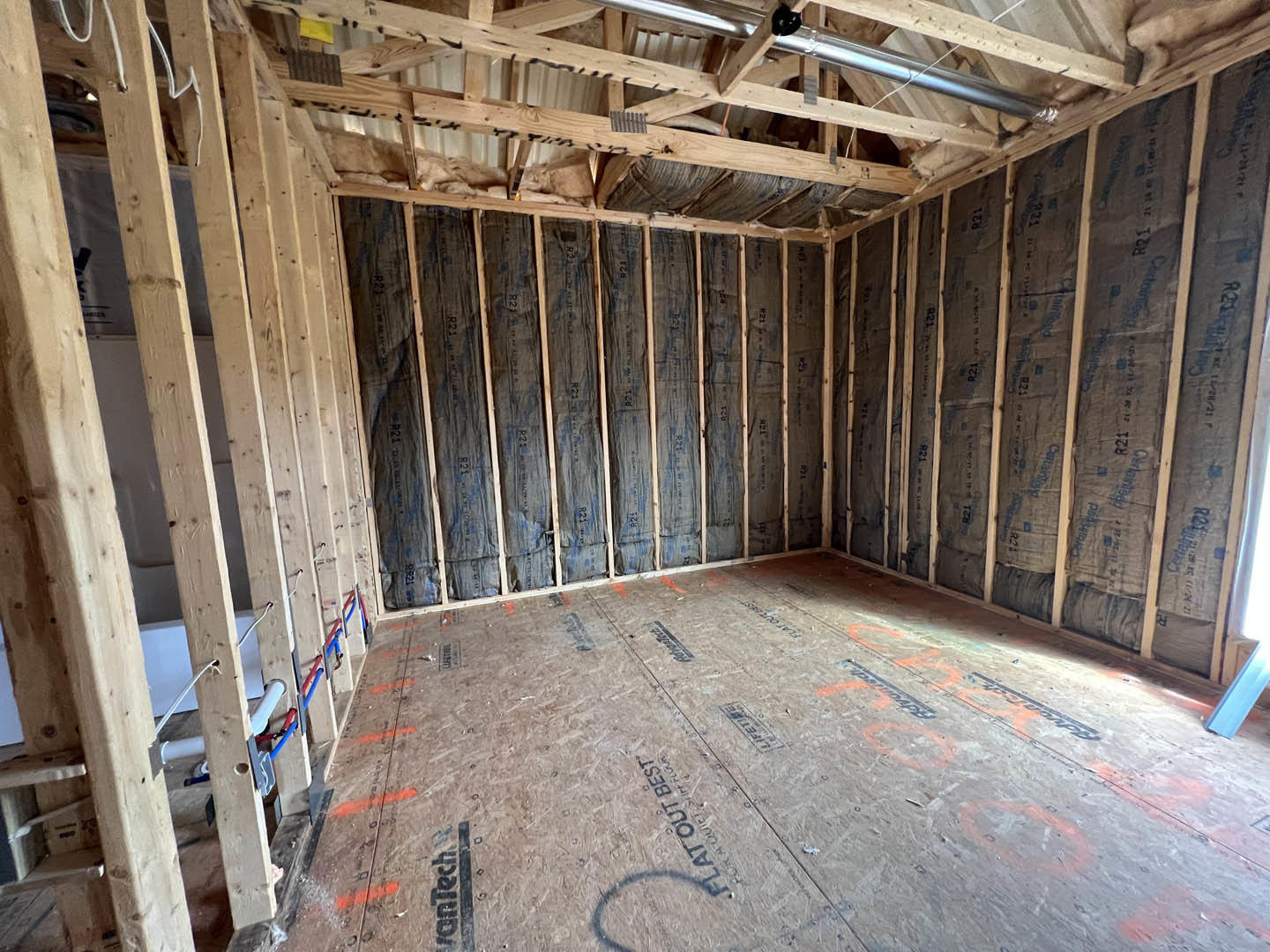 Room under construction with exposed wood walls, ceiling beams, and visible insulation