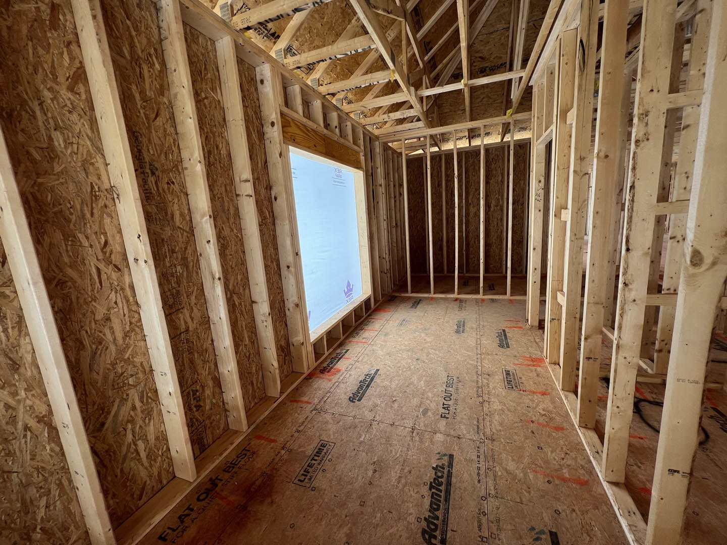 Wood-framed room under construction with exposed beams, insulation, and a window set in an unfinished wall