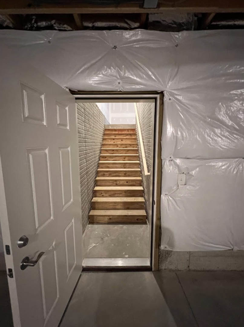 White door opening to corner wooden staircase, plaster walls, light wood flooring, minimal interior finishes