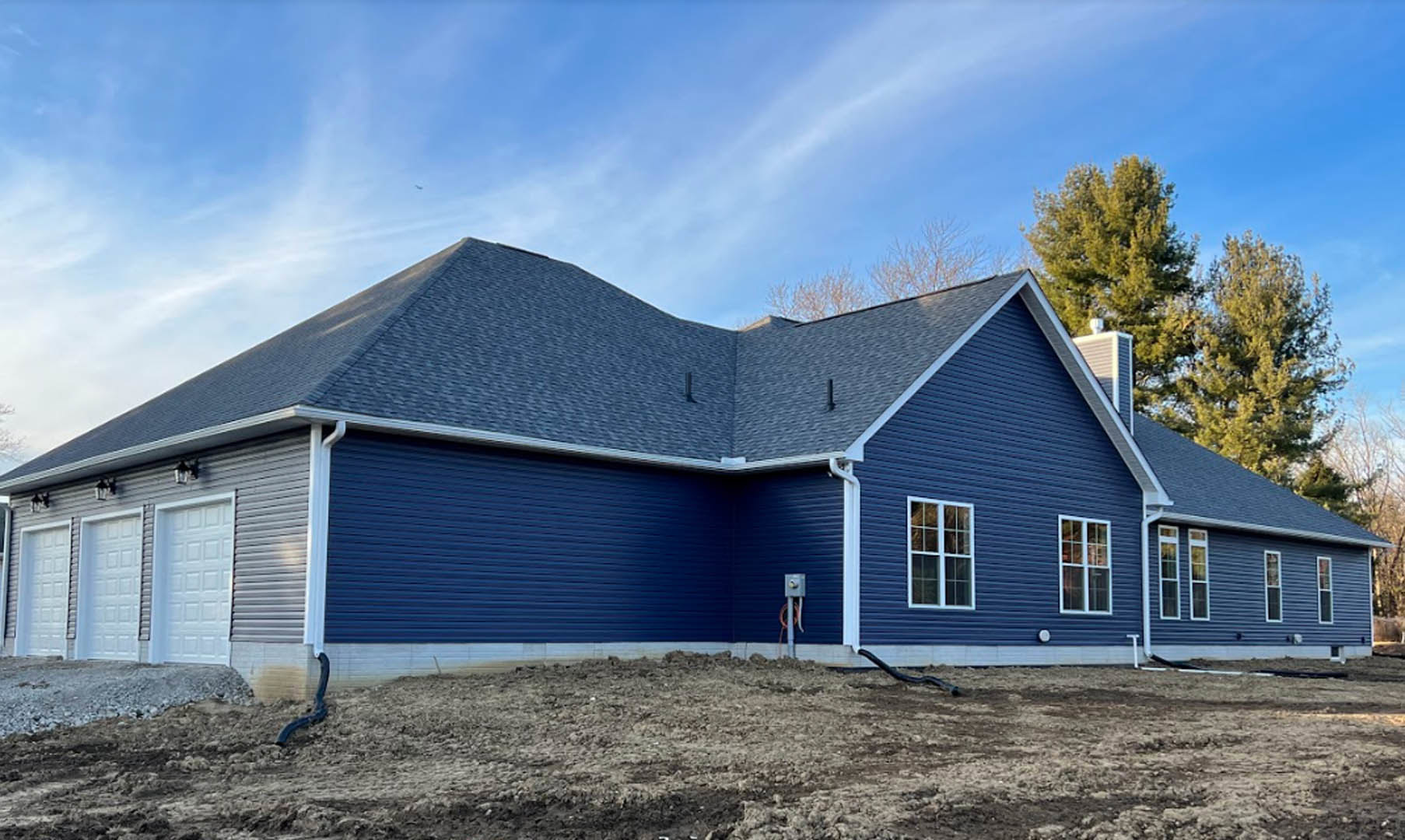 Blue siding exterior with white roof, white garage door featuring square tile pattern, close-up window, trees in background, partly cloudy sky