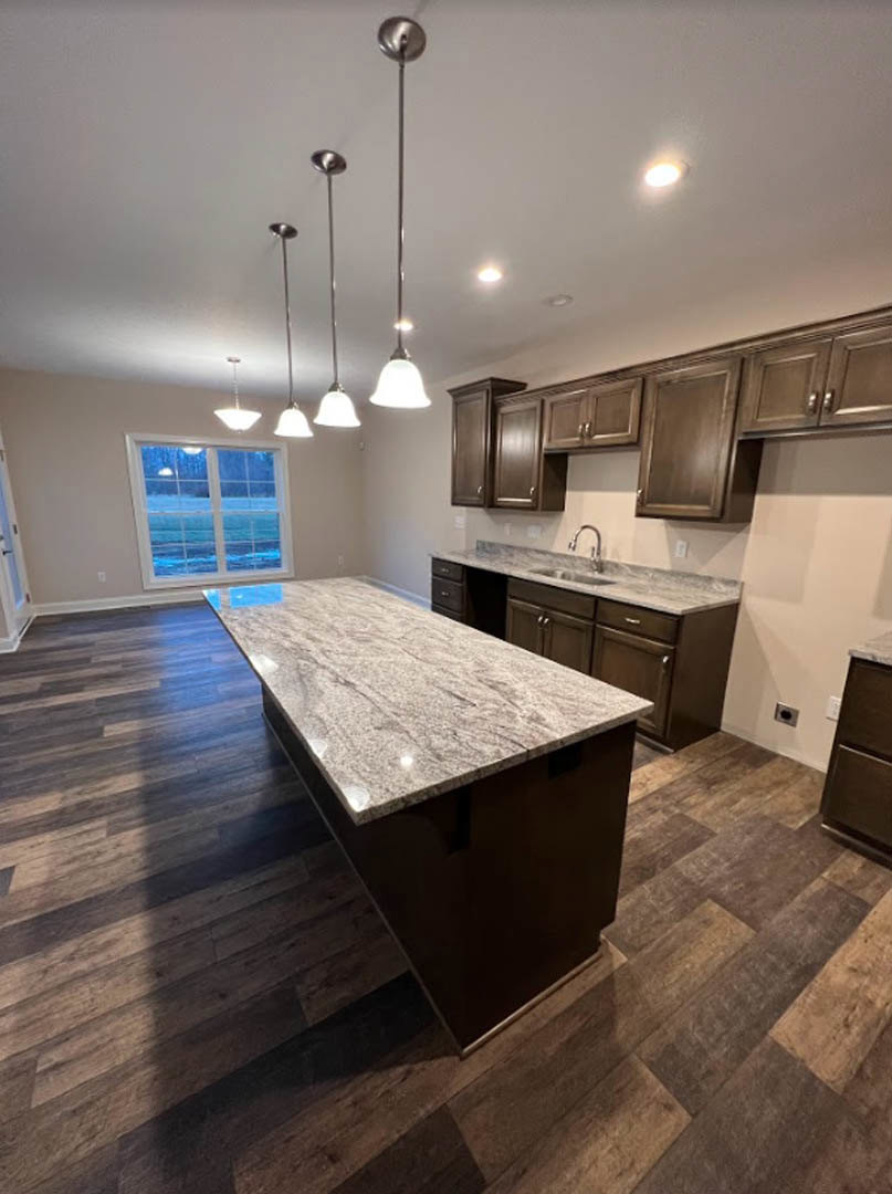 Marble kitchen island with waterfall edge, white tile backsplash, light wood cabinetry, stainless steel fixtures, ocean view through large window, recessed ceiling lights, light