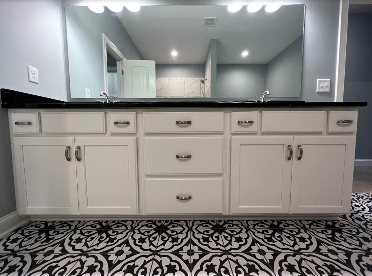 Bathroom with black and white tile floor, white cabinetry with silver handles, wall-mounted mirror, white door, tiled wall, dual light switch, and close-up of a drawer.