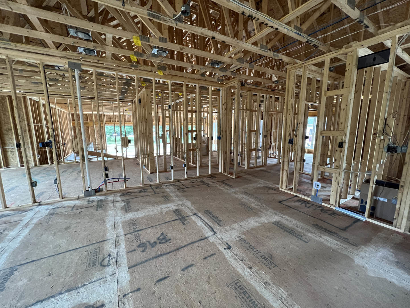 Exposed wood framing and beams inside a house under construction, unfinished subfloor with black markings, open interior space
