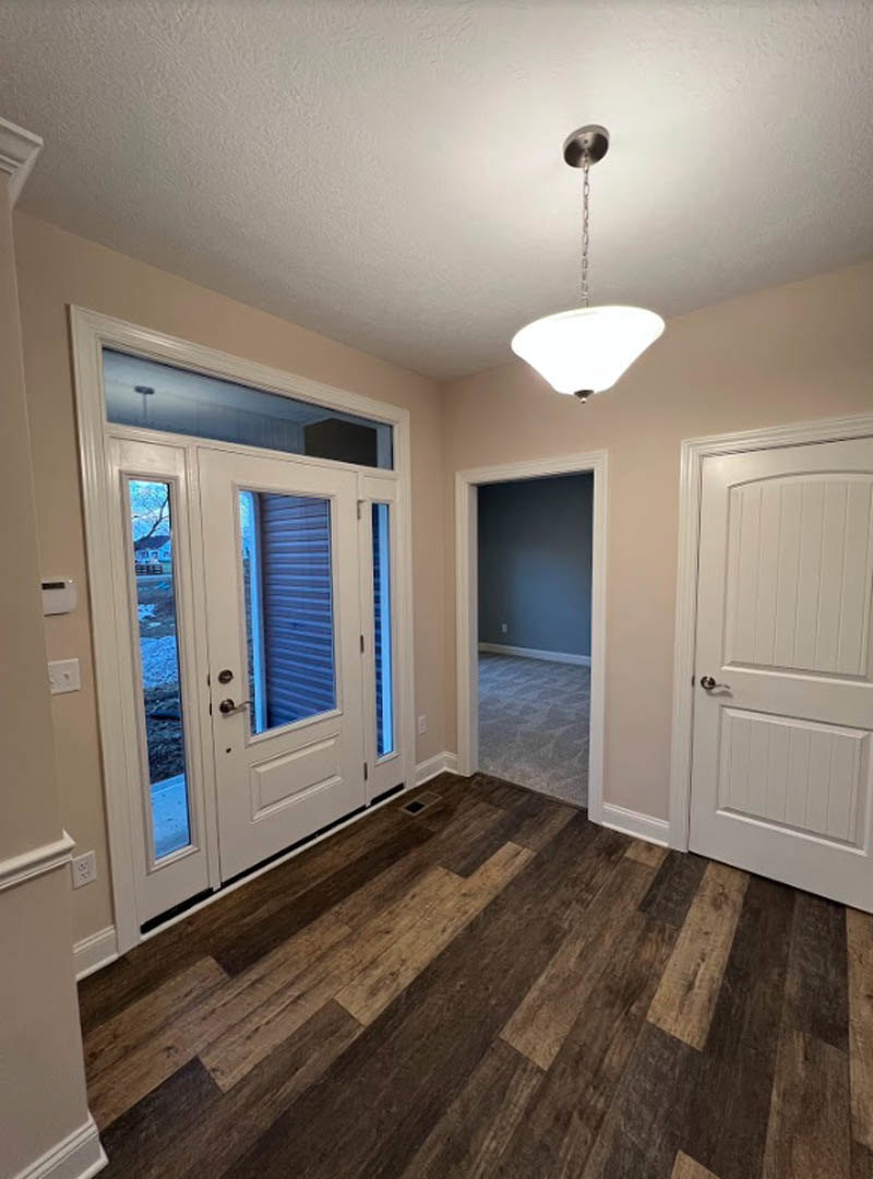 Hallway with wood flooring, white paneled doors featuring silver handles, white walls, and a ceiling-mounted lamp.