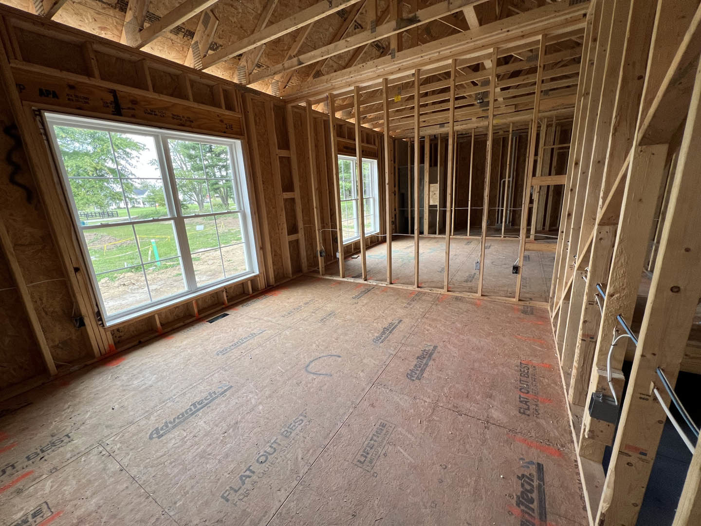 Wood-framed room under construction with exposed beams, unfinished floor, and large window allowing daylight