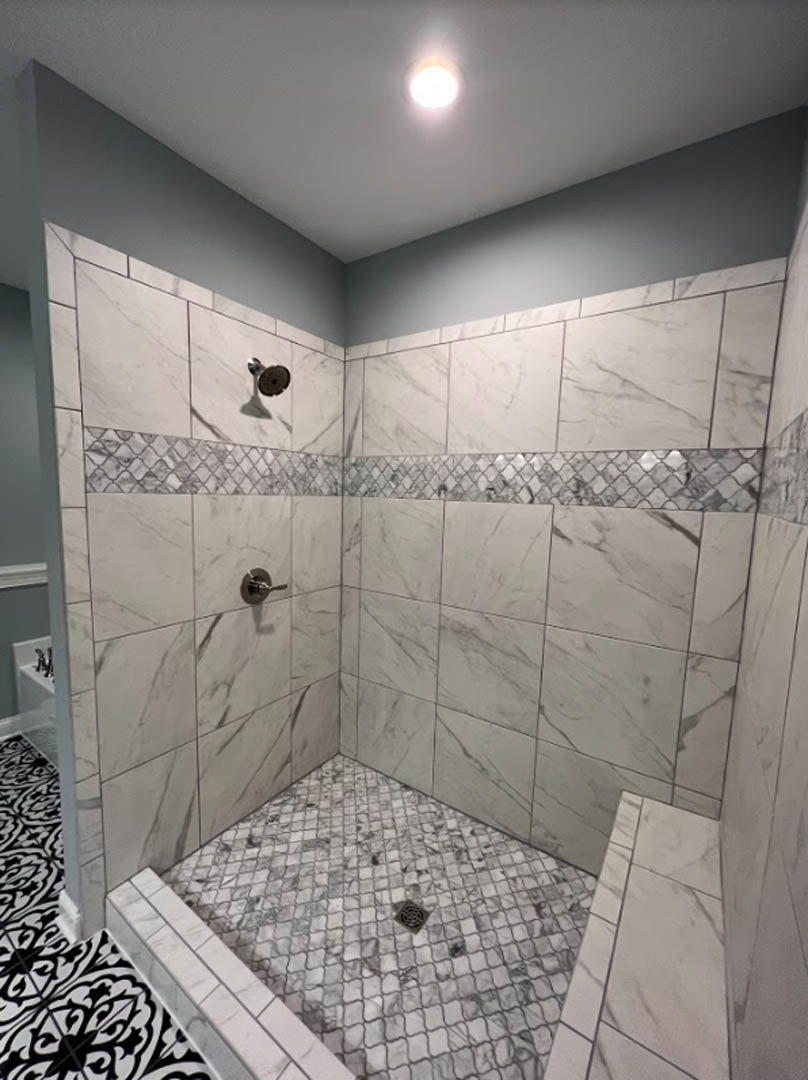 Shower with marble tile walls, chrome shower head, and white tile floor with black lines and central drain
