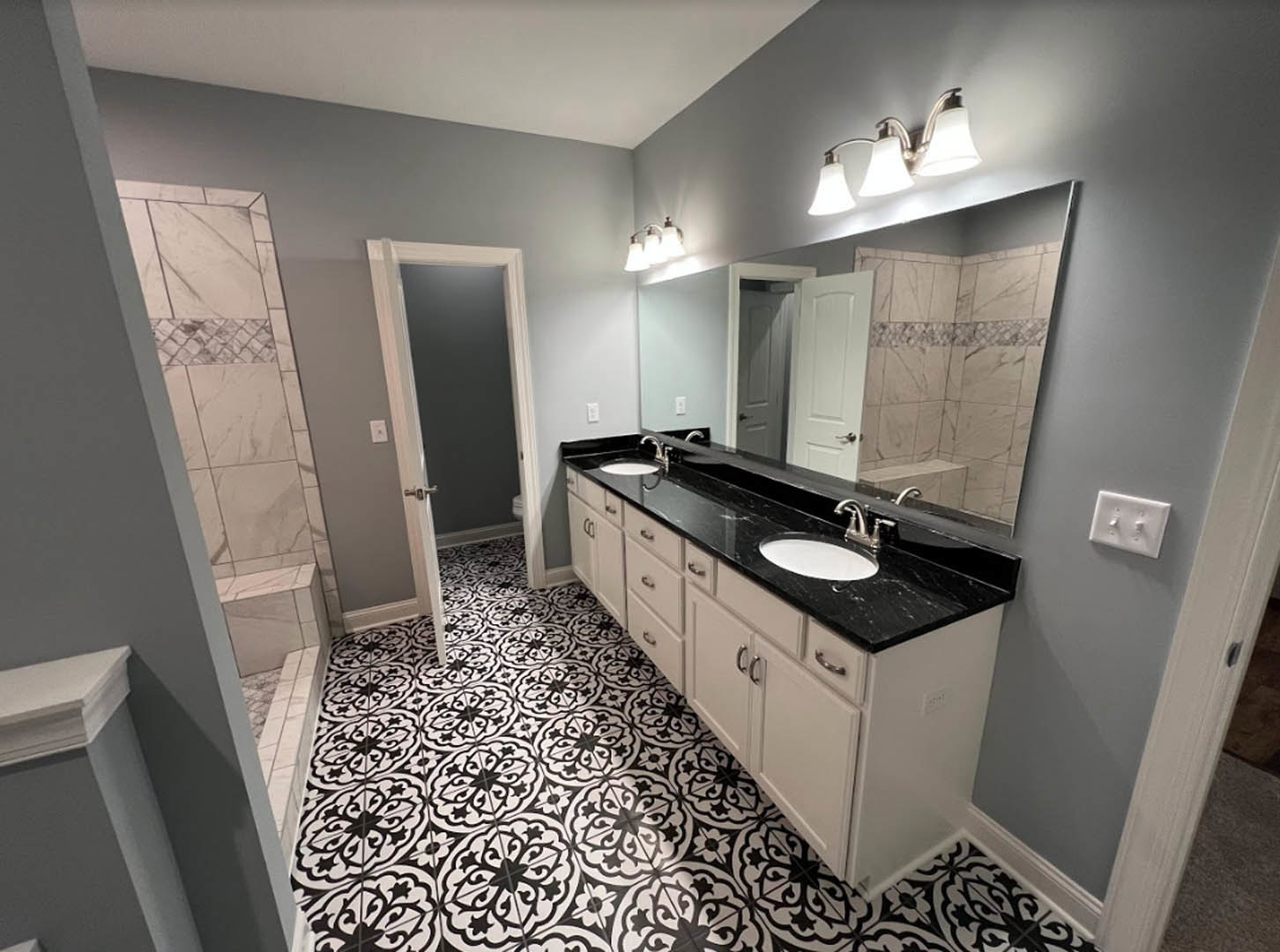 Bathroom with black and white tile floor, white walls, wall-mounted light switch, open door, chrome faucet, white countertop, cabinetry, and mirror above sink