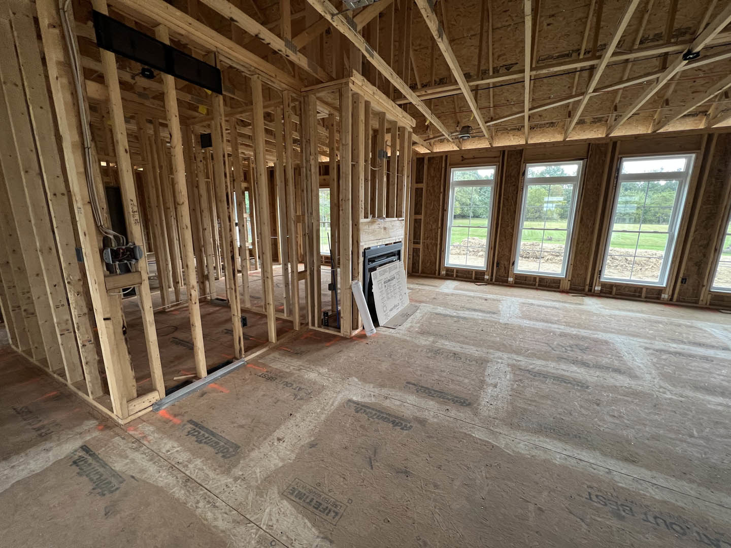 Room under construction with exposed wood framing, large windows, ceiling beams, and unfinished floor