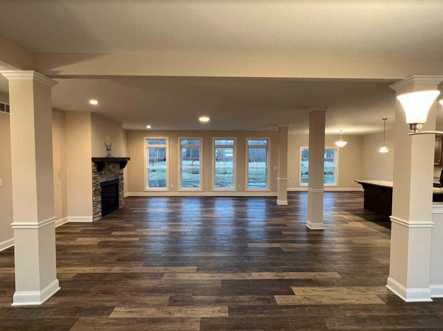 Spacious living room featuring stone fireplace, white column, multiple windows, laminate flooring, and decorative molding.