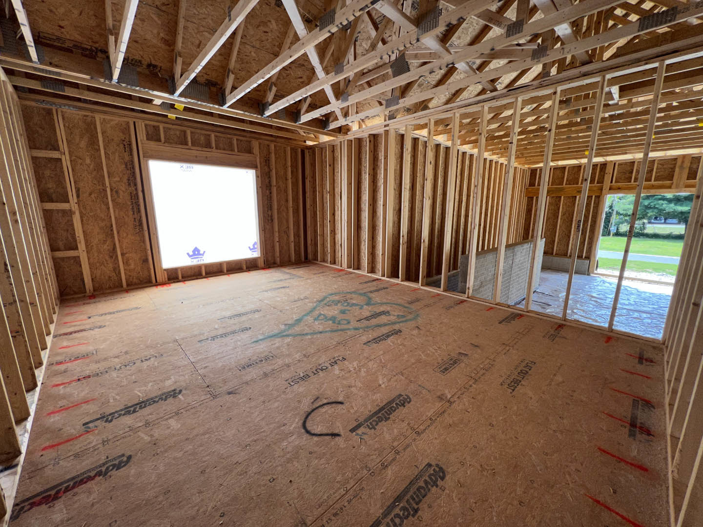 Unfinished room with exposed wood ceiling beams, framed window, and construction materials on subfloor