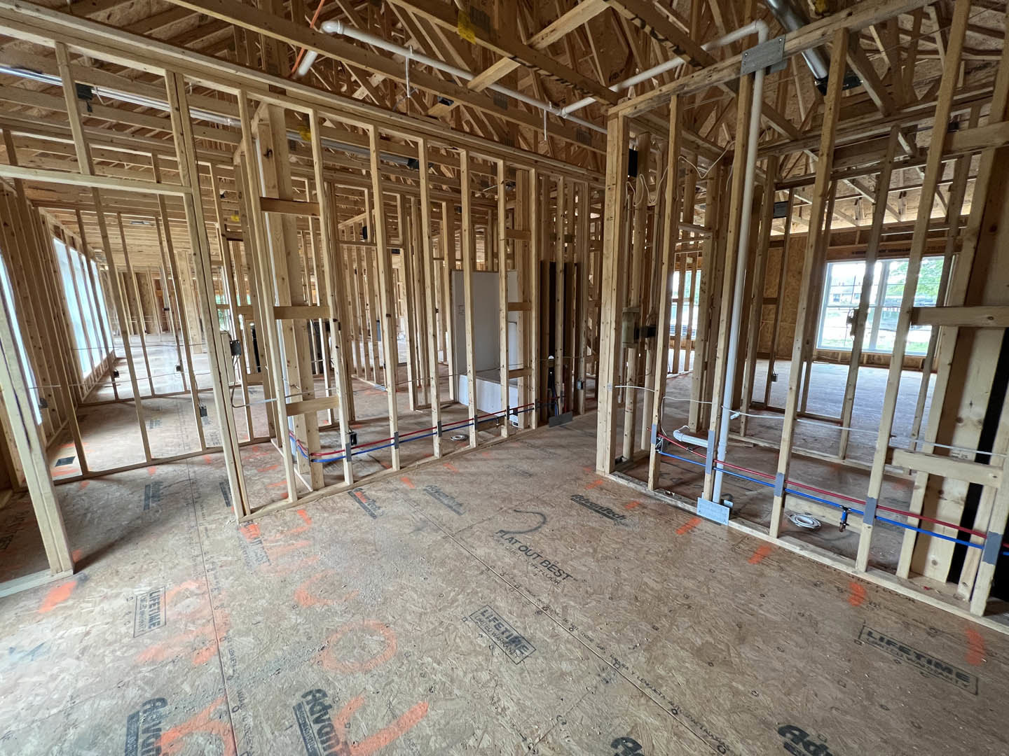Exposed wood framing and beams in a partially constructed room with visible floor, window, roof detail, and plumbing pipes