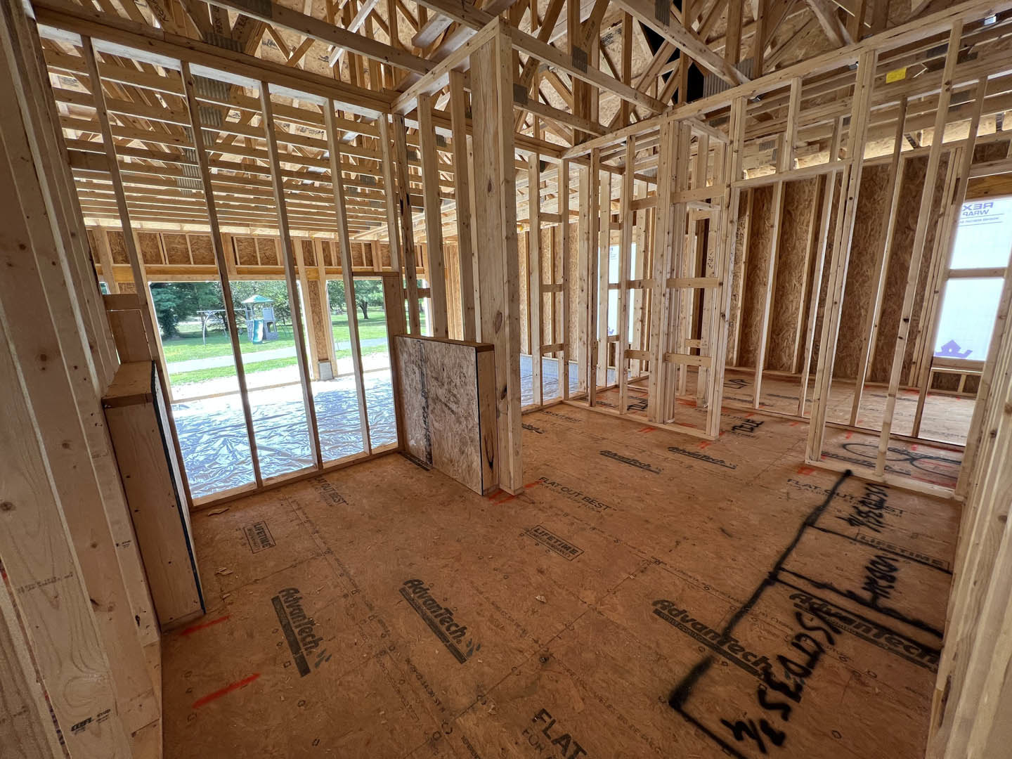 Exposed wood ceiling beams, unfinished wood floor with black construction markings, large window letting in daylight, interior under construction