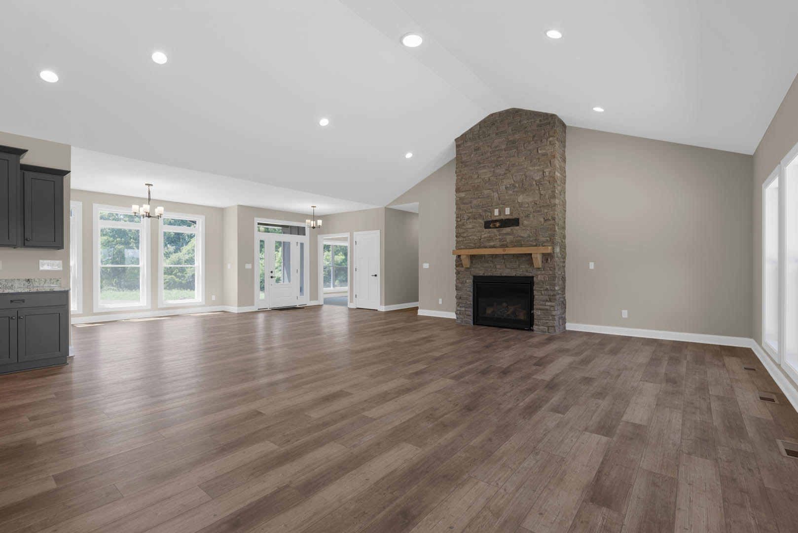 Spacious living room featuring stone fireplace with glass door and wood mantel, hardwood flooring, white ceiling, and built-in cabinetry