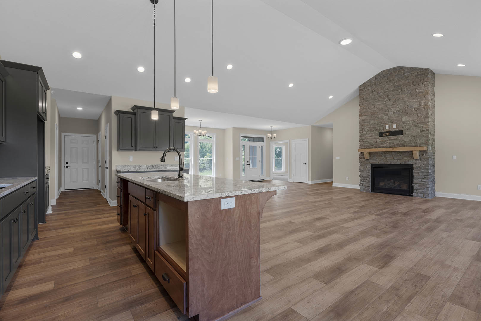 Open kitchen and living room featuring a stone fireplace with glass door and wood mantel, kitchen island with built-in sink, white cabinetry with black handles, wood beam accents