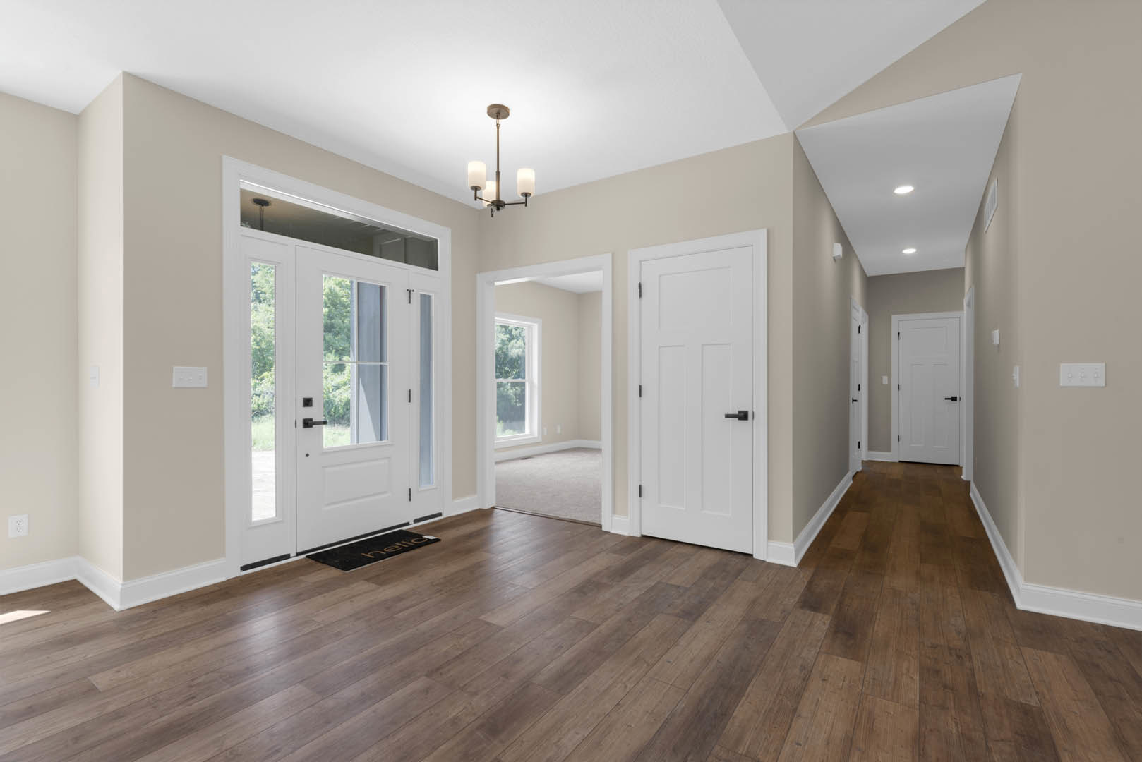 Hallway with white paneled doors featuring black handles, hardwood flooring, white walls, black and gold door mat, and a white door with glass window panes