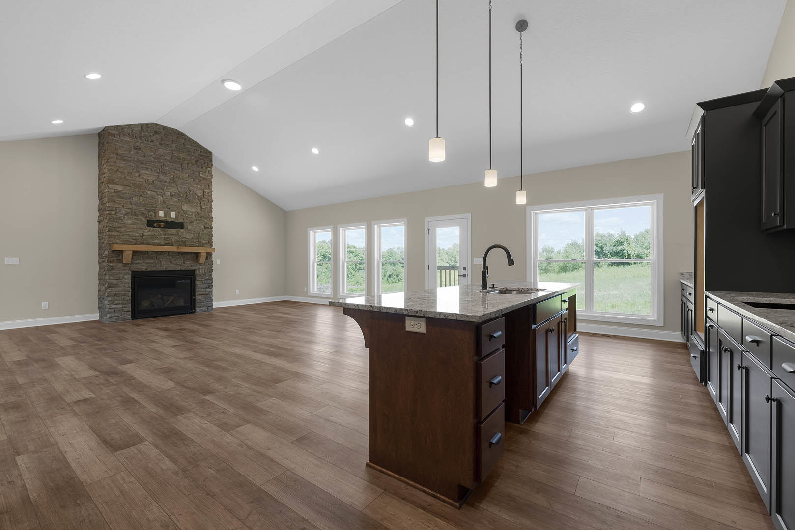 Spacious open floor plan featuring a kitchen island with marble countertop, sink, and drawers, adjacent to a stone fireplace with wood mantel and glass door; kitchen includes