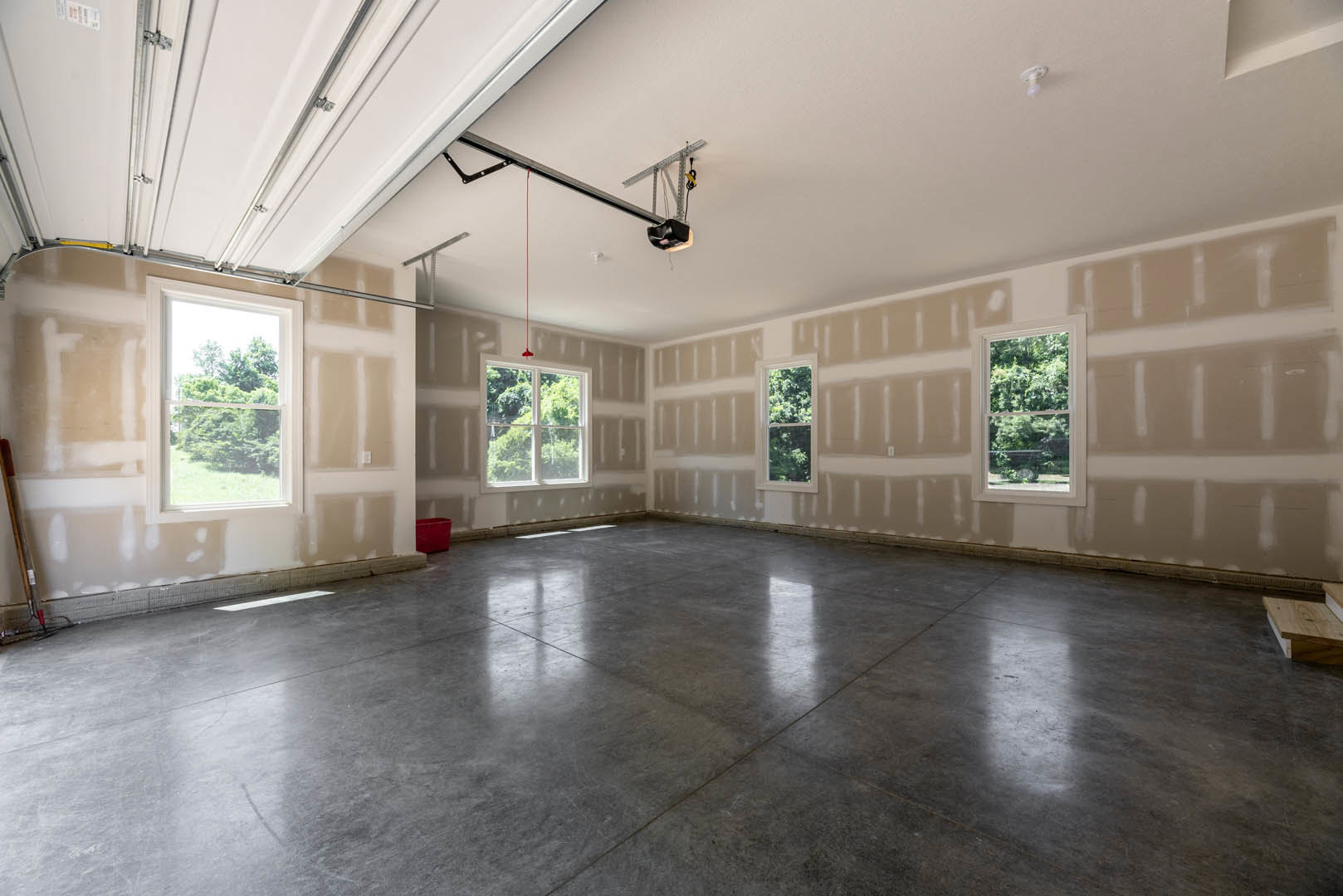Concrete floor with a red plastic bin, white walls, large windows overlooking trees, natural daylight filling the room