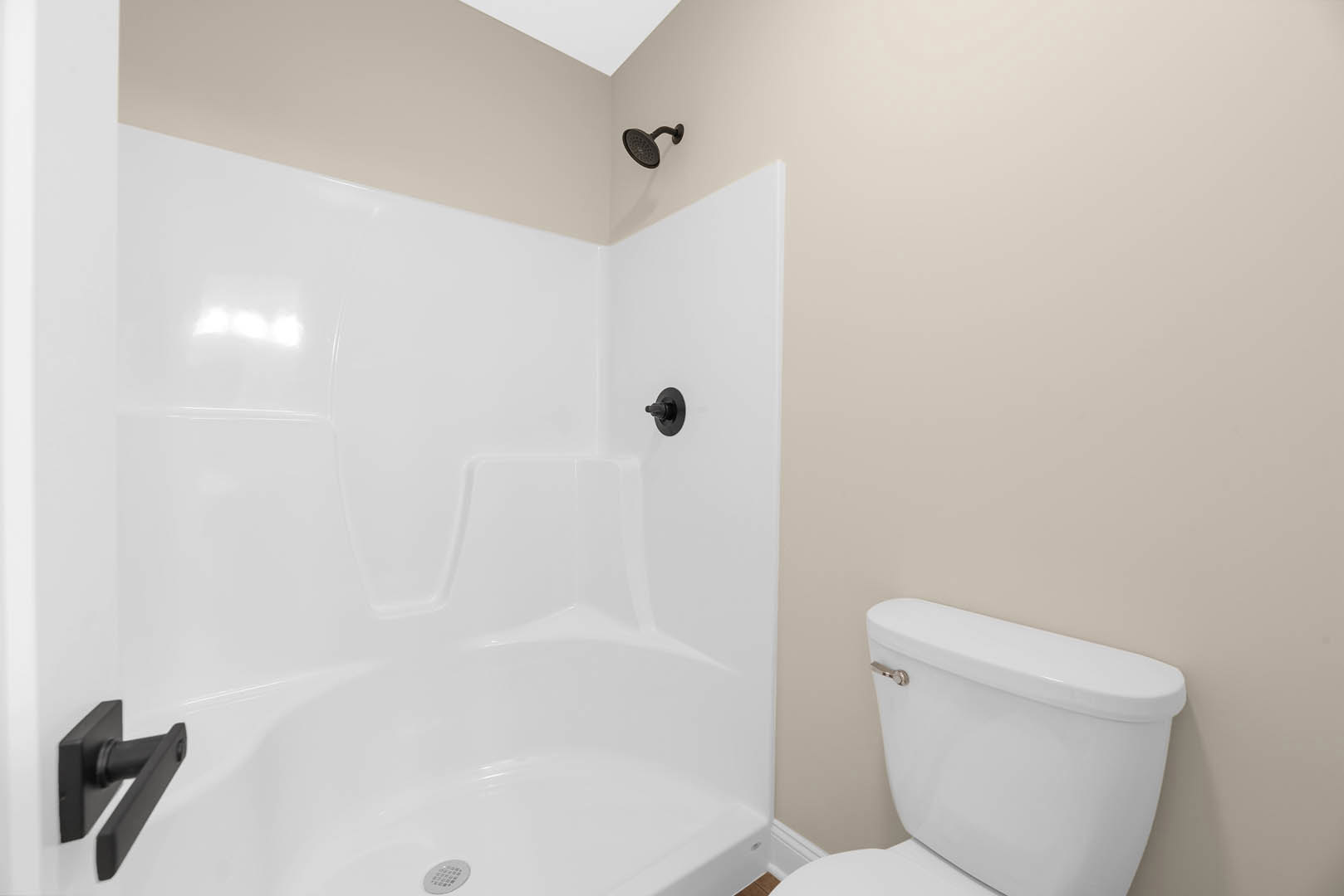 Bathroom with white tile walls, glass shower enclosure, wall-mounted shower head, white toilet, freestanding white bathtub with black handles, and black hardware accents on doors