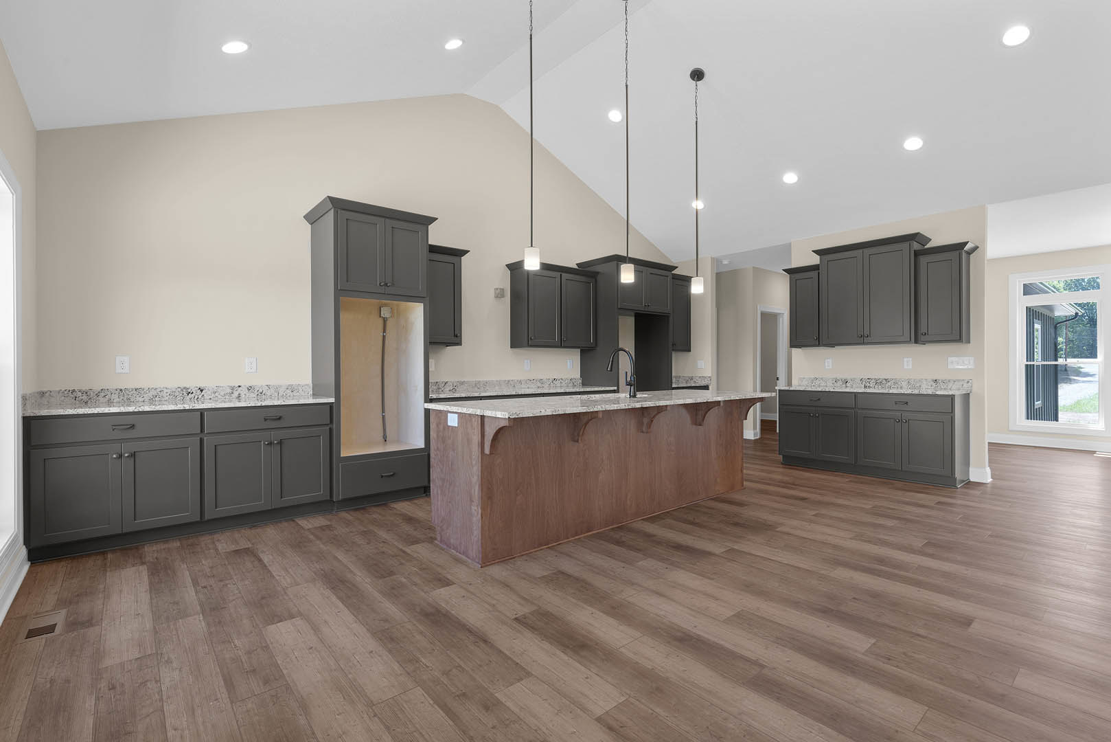 Spacious kitchen featuring a large marble-topped island, wood flooring, white cabinetry, stainless steel sink, and windows overlooking the exterior of the home.
