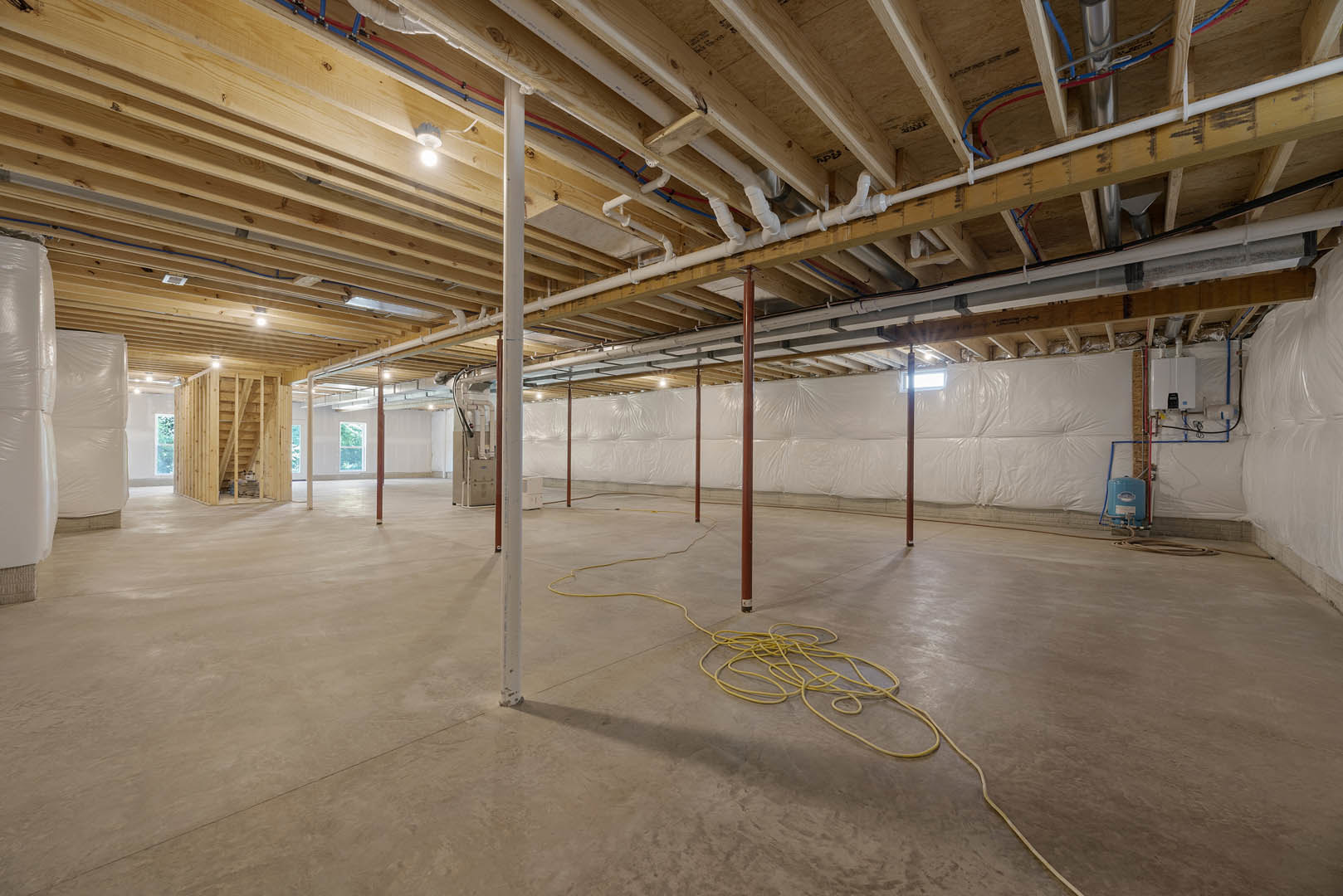 White-walled room with exposed ceiling pipes, white tile floor, yellow cable or rope on the ground, and brown pole near a white bed