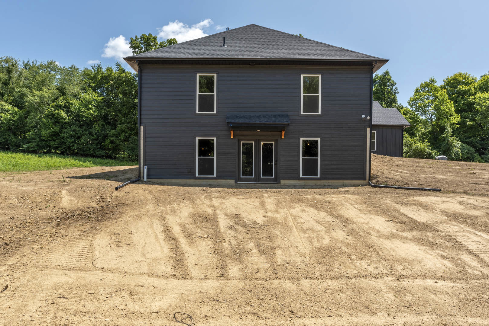 Modern home with white-framed windows, double glass doors, and exterior lights, set on a dirt lot with a small hill and sparse landscaping.