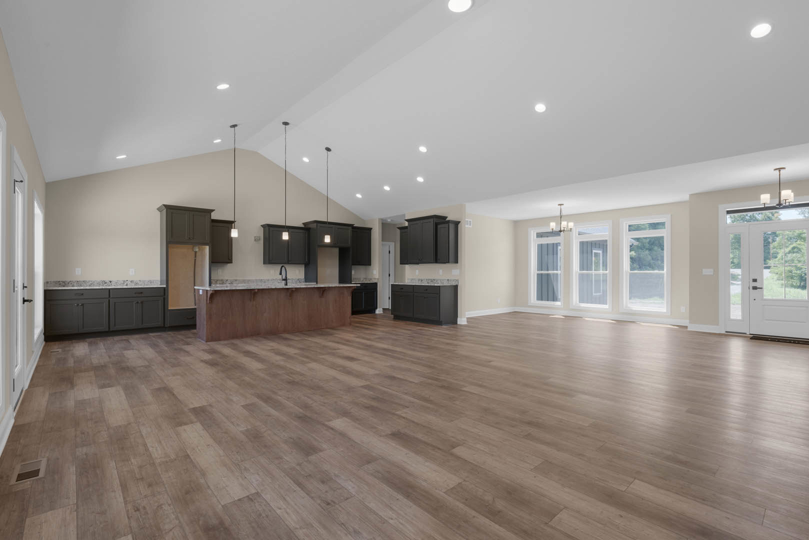Spacious open floor plan featuring hardwood flooring, central kitchen island with marble countertop, recessed lighting in white ceiling, glass-paneled white door, and large window