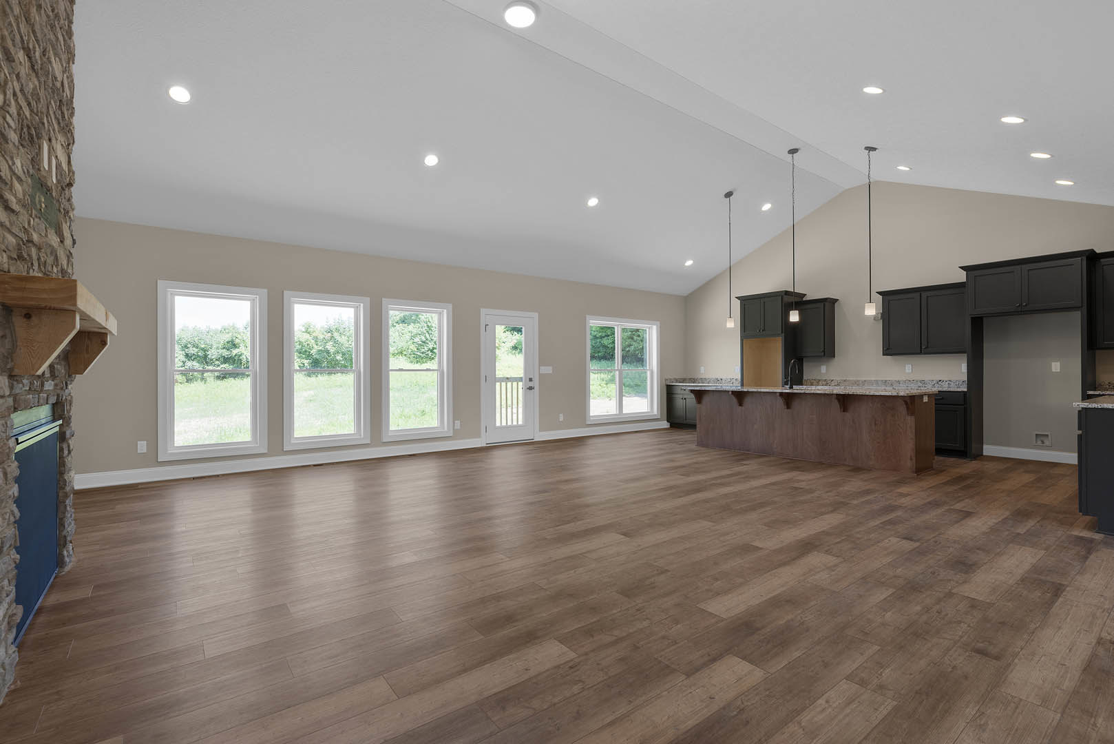 Open-concept room featuring hardwood floors, central kitchen island with marble countertop, white cabinetry, large windows with white frames overlooking trees, and a white door