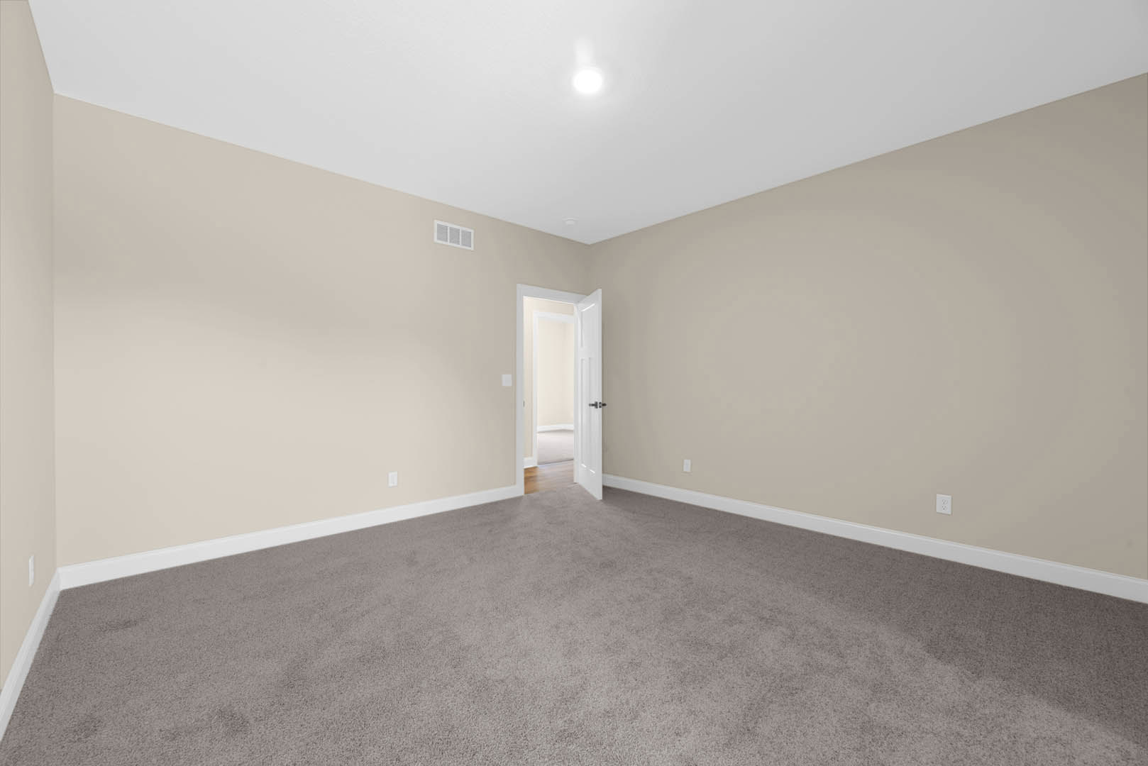 Carpeted room with white walls, open white door featuring a black handle, white ceiling, and natural light illuminating the space
