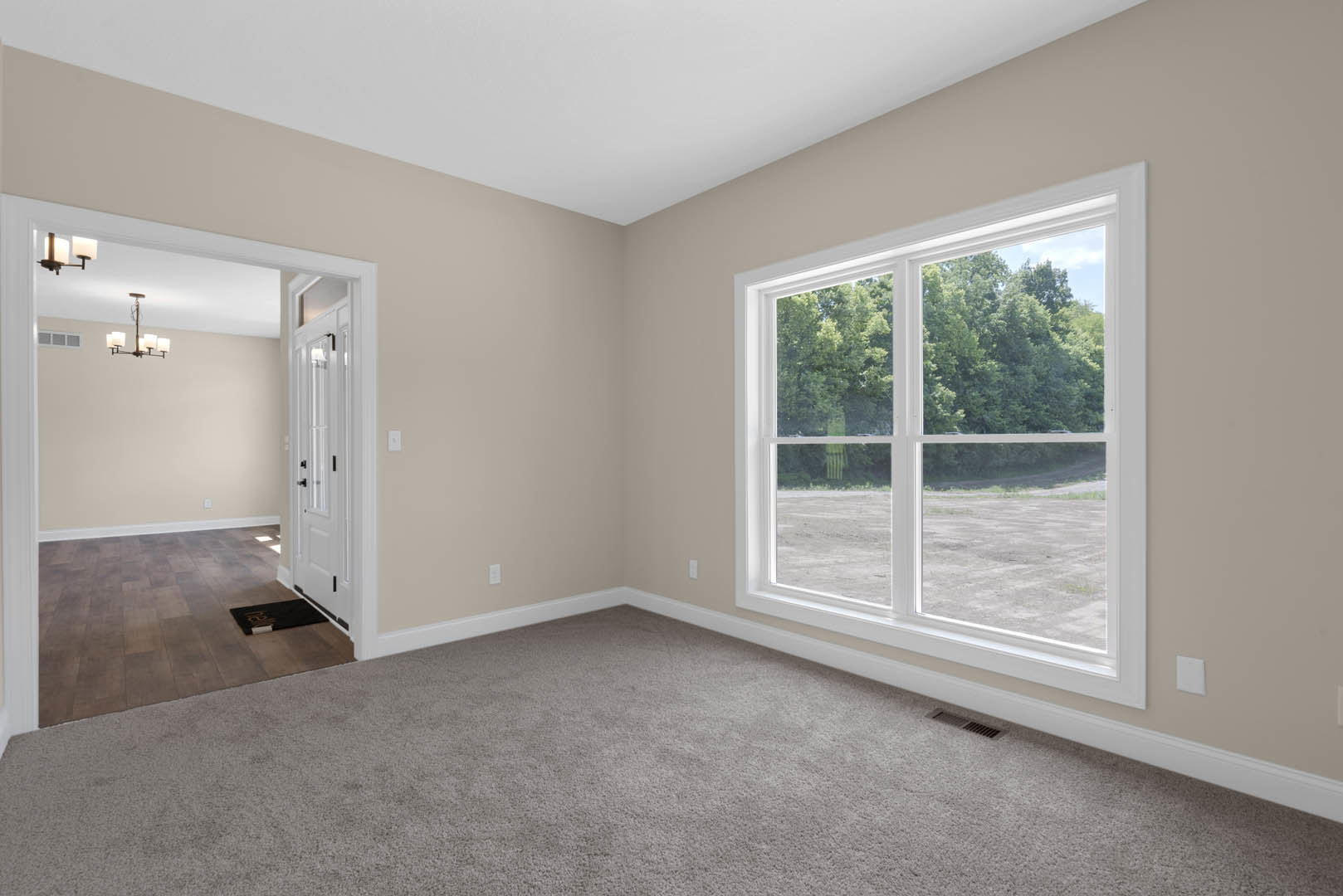 Bedroom with beige carpet, large window overlooking trees, white walls, and wood trim