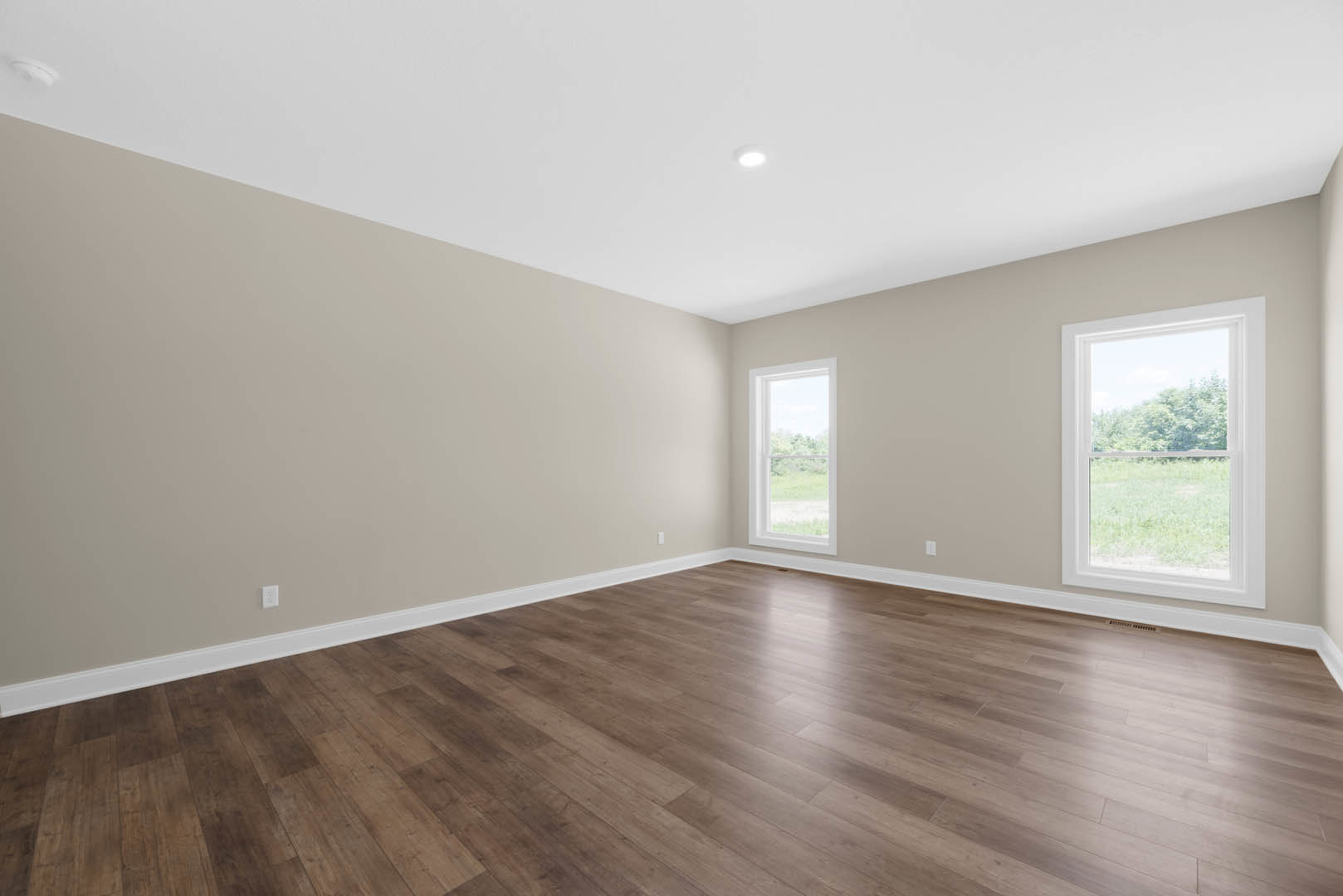 Spacious room with hardwood flooring, large windows overlooking grassy yard and tree-filled field, white ceiling with round light fixture