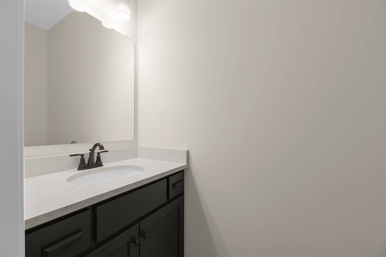 White bathroom vanity with black faucet and handles, rectangular mirror above sink, white countertop, light fixtures mounted on white wall, tile backsplash, cabinetry with drawers.