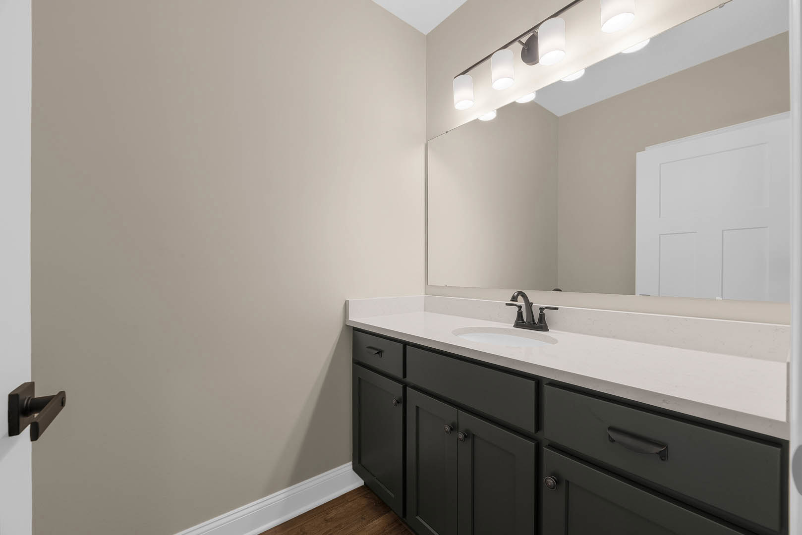 Modern bathroom featuring a rectangular mirror above a white sink with chrome faucet, light gray tile backsplash, white cabinetry, and a row of ceiling lights; white paneled door