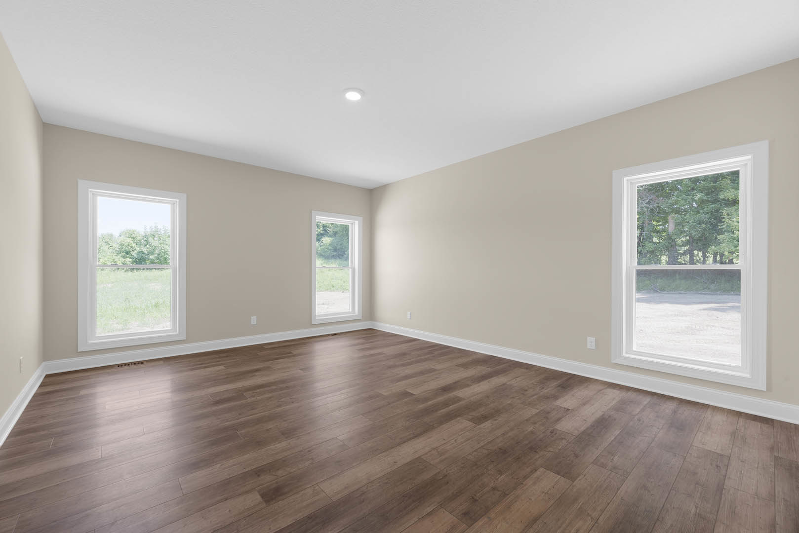 White walls and wood flooring in a room with large windows overlooking grass and trees