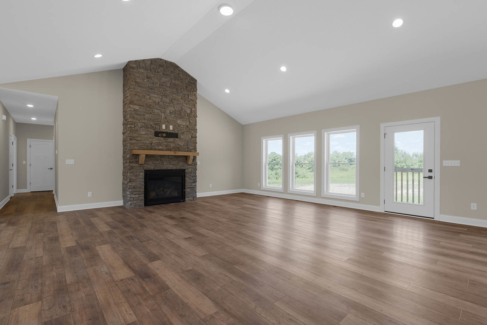 Spacious living area with stone fireplace featuring glass door and wood mantel, hardwood flooring, white door with silver handle, and adjacent glass door with railing