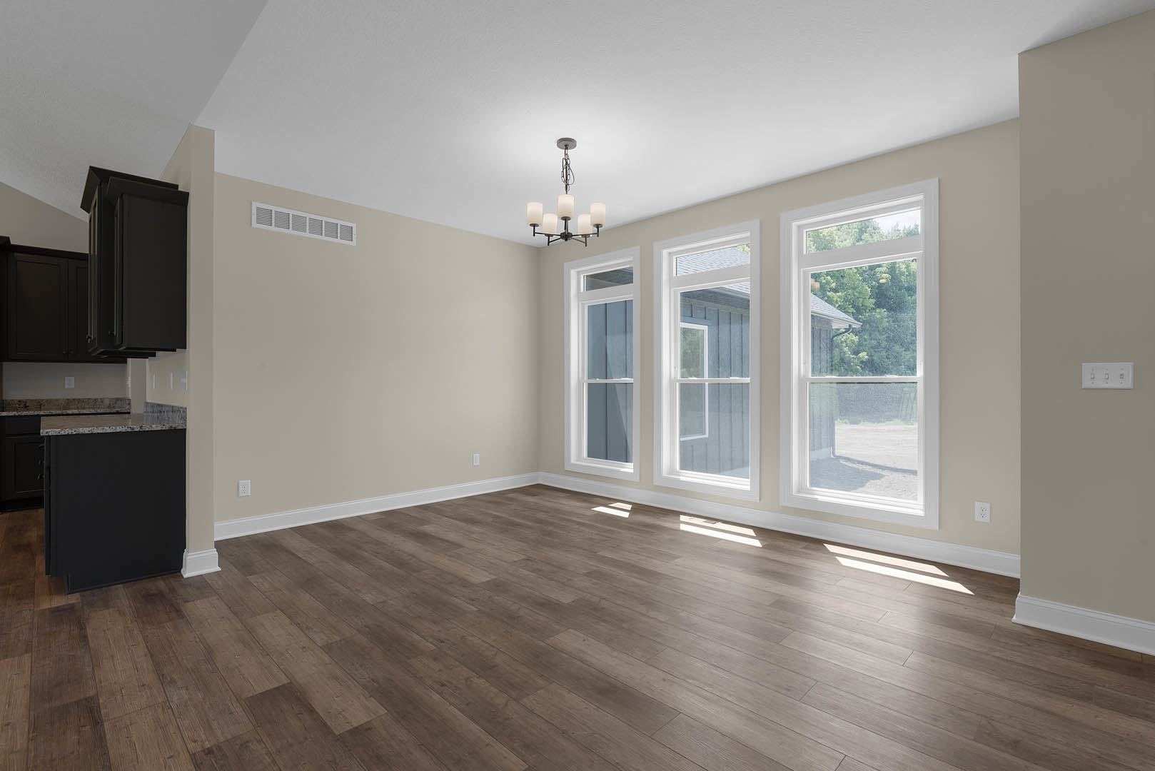 Spacious room with wood flooring, white walls, large windows overlooking trees, black rectangular island with marble countertop, modern chandelier