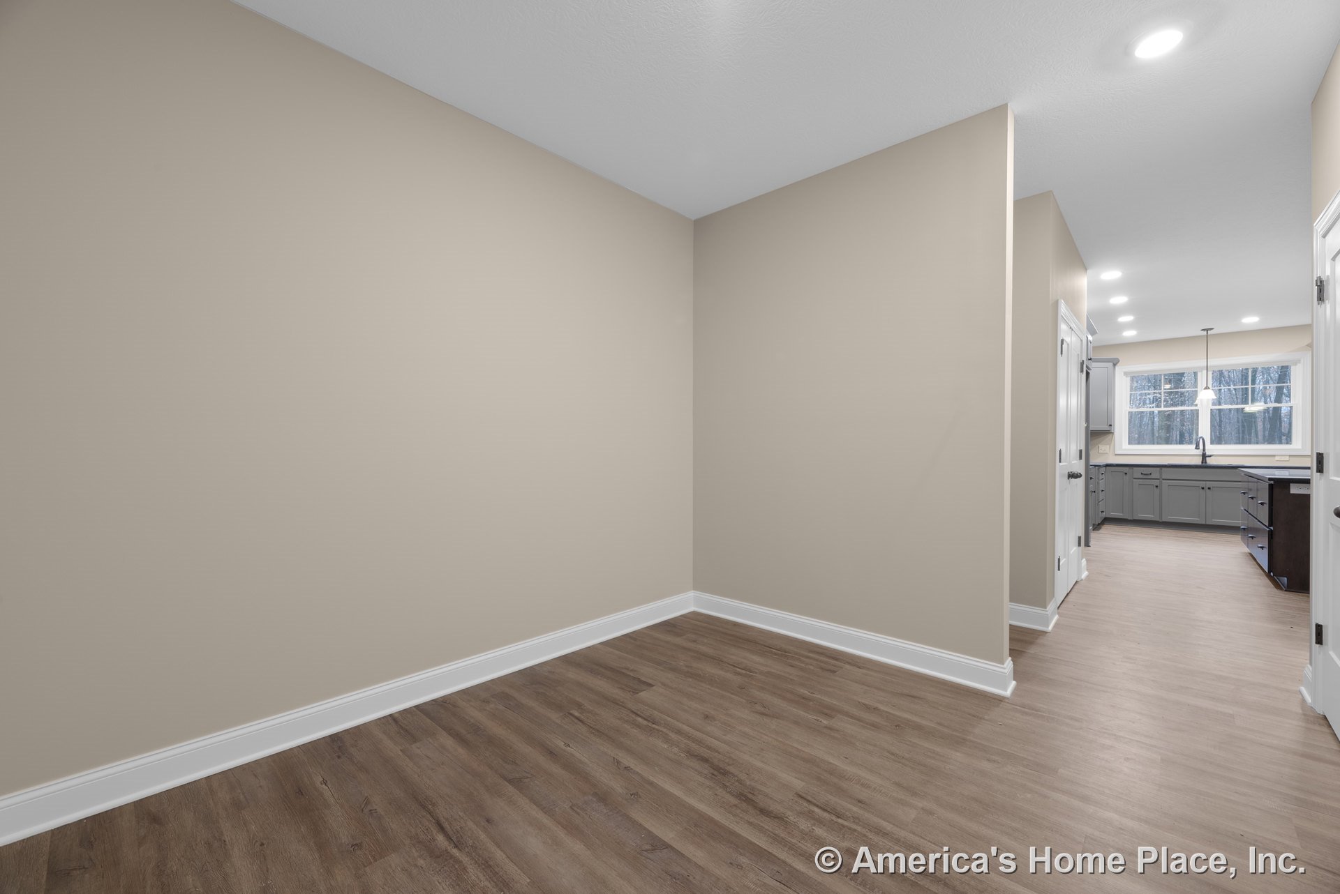 Open floor plan featuring wood-look plank flooring, beige walls with white baseboard trim, recessed ceiling lights, gray kitchen cabinetry, and a large window above the sink.
