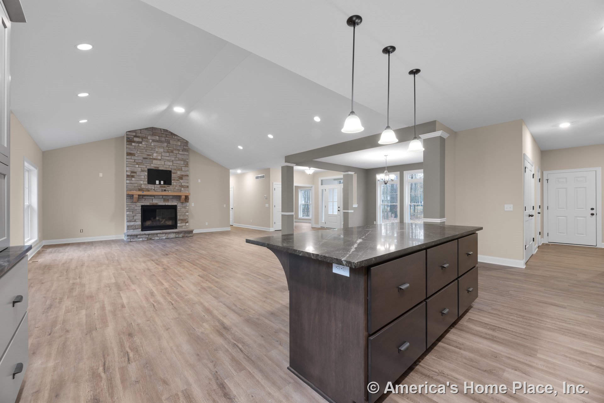 Stone fireplace with wood mantel and recessed lighting under a vaulted ceiling, open floor plan connecting living room and kitchen, dark wood kitchen island with granite