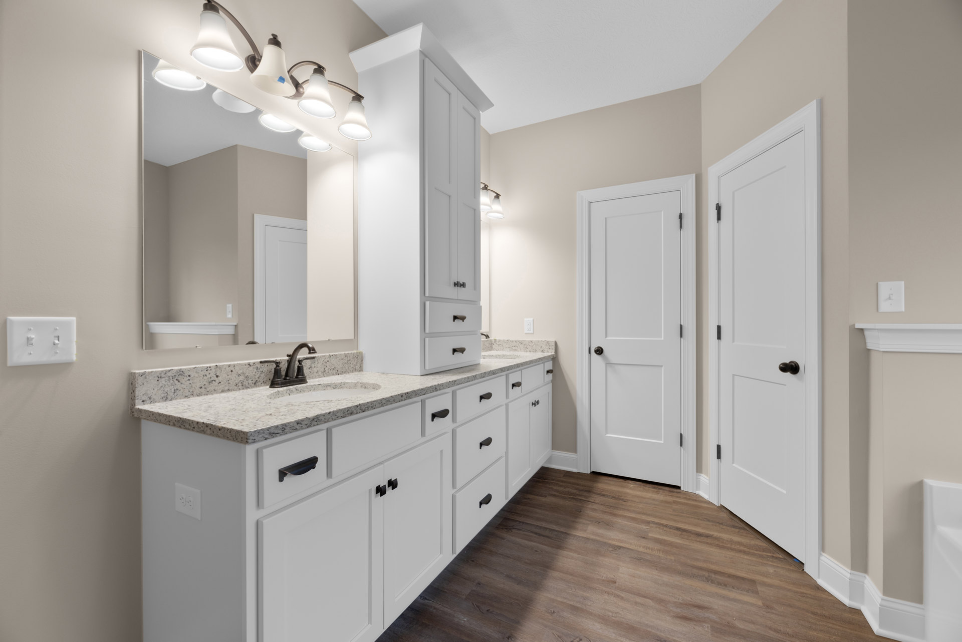 Bathroom with white cabinets, white doors featuring black knobs, wood flooring with white trim, ceiling light fixture illuminated, and light switch on the wall.