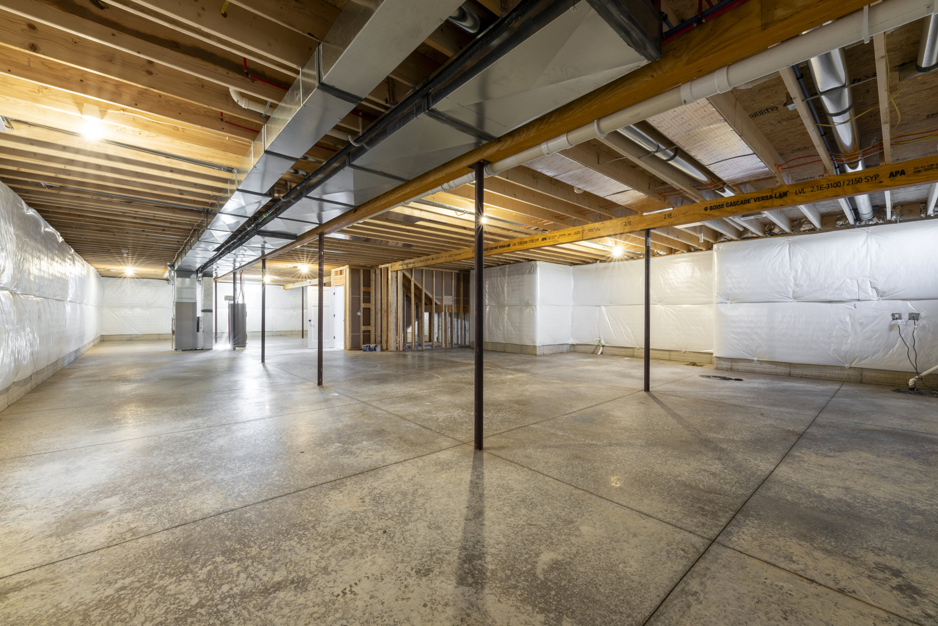 Empty basement room with exposed ceiling pipes, concrete floor, white walls, and structural pole