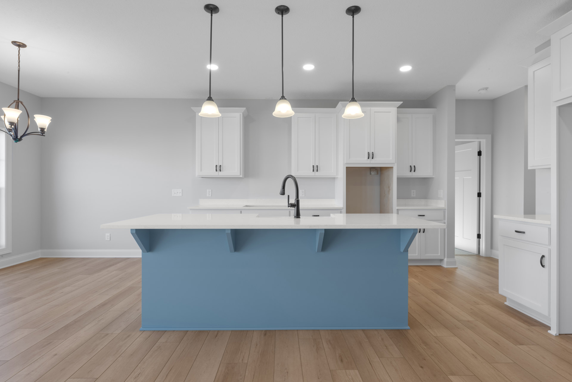 Blue kitchen island with white cabinets, white countertop, black faucet, tile backsplash, pendant light fixture, hardwood flooring