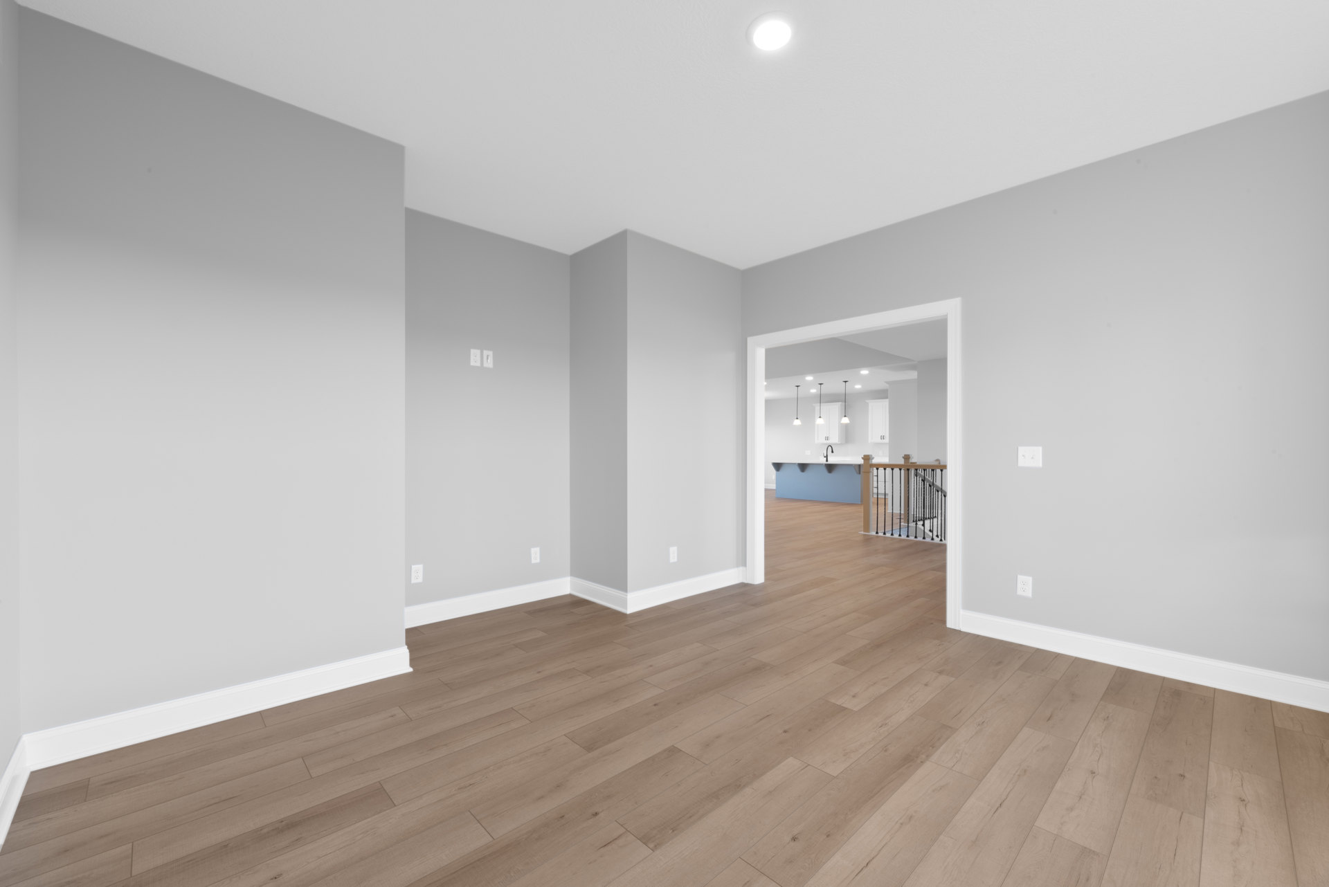 Hardwood floor with white trim, open door leading to adjacent room, recessed ceiling light, close-up view of staircase with wood steps and white risers.